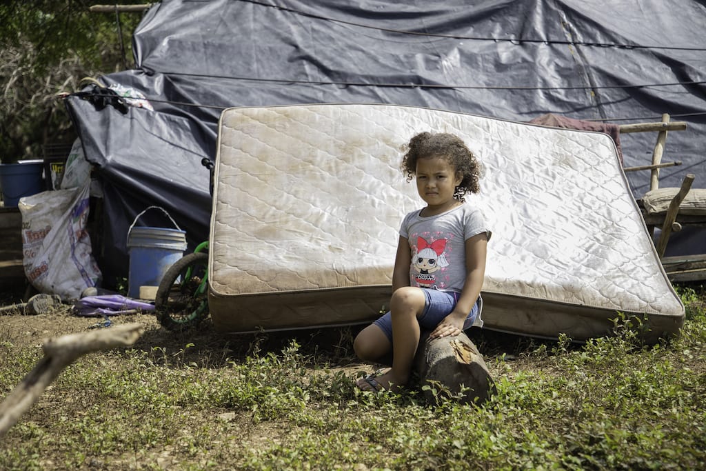 A girl sits on a log, in front of a mattress.